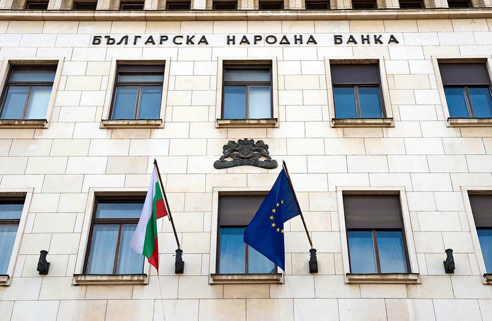 Сучасна будівля болгарського банку з класичним фасадом, колонами та симетричною архітектурою під ясним блакитним небом.