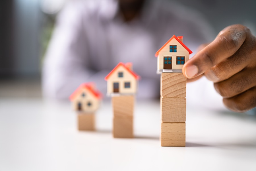 Рука вибудовує моделі будинків на дерев'яних блоках, показуючи градацію цін та ризики ринку котловану в Болгарії.